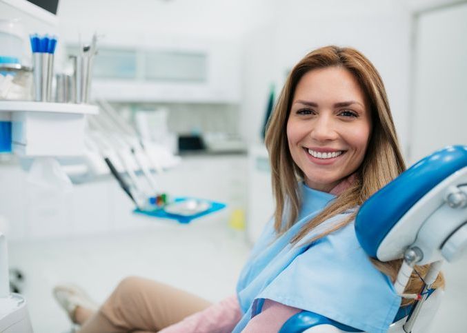 A woman is smiling while sitting in a dental chair.