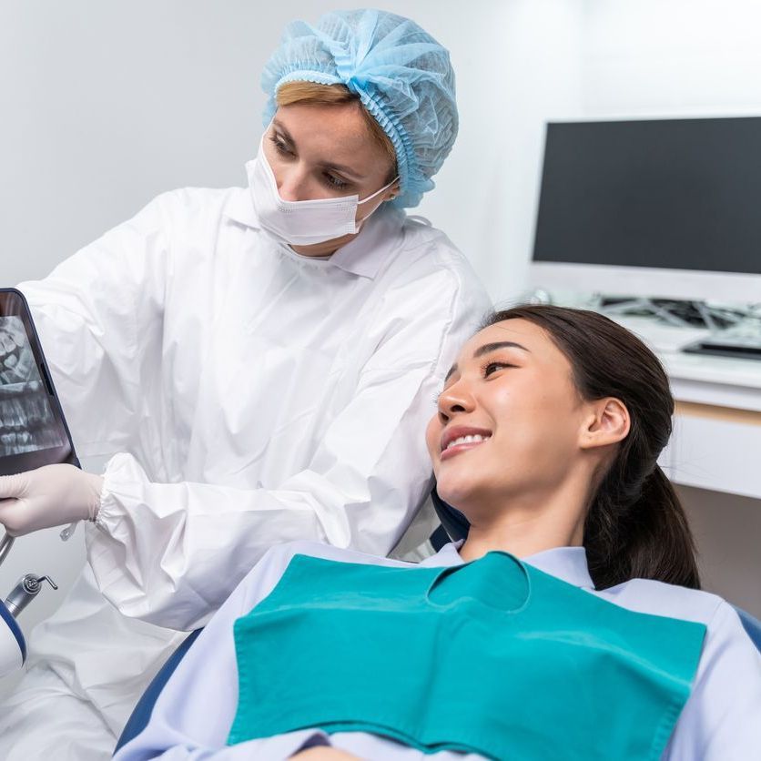 A woman is sitting in a dental chair while a dentist examines her teeth.