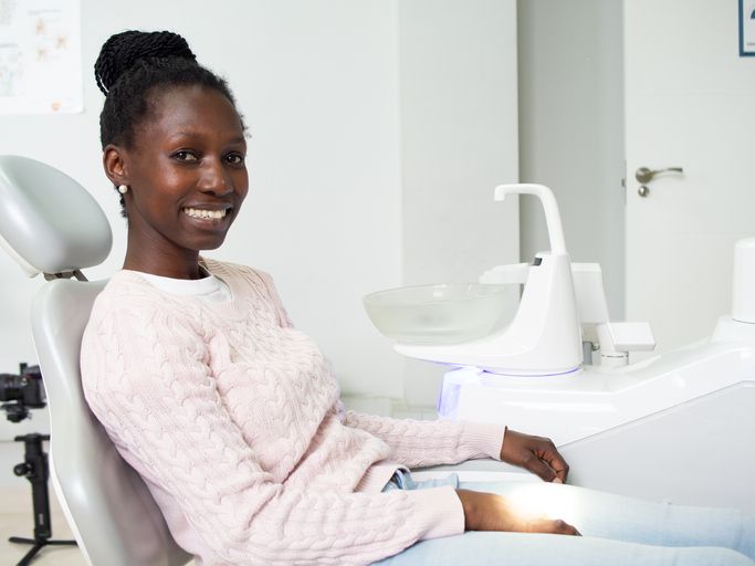 A woman is smiling while sitting in a dental chair.