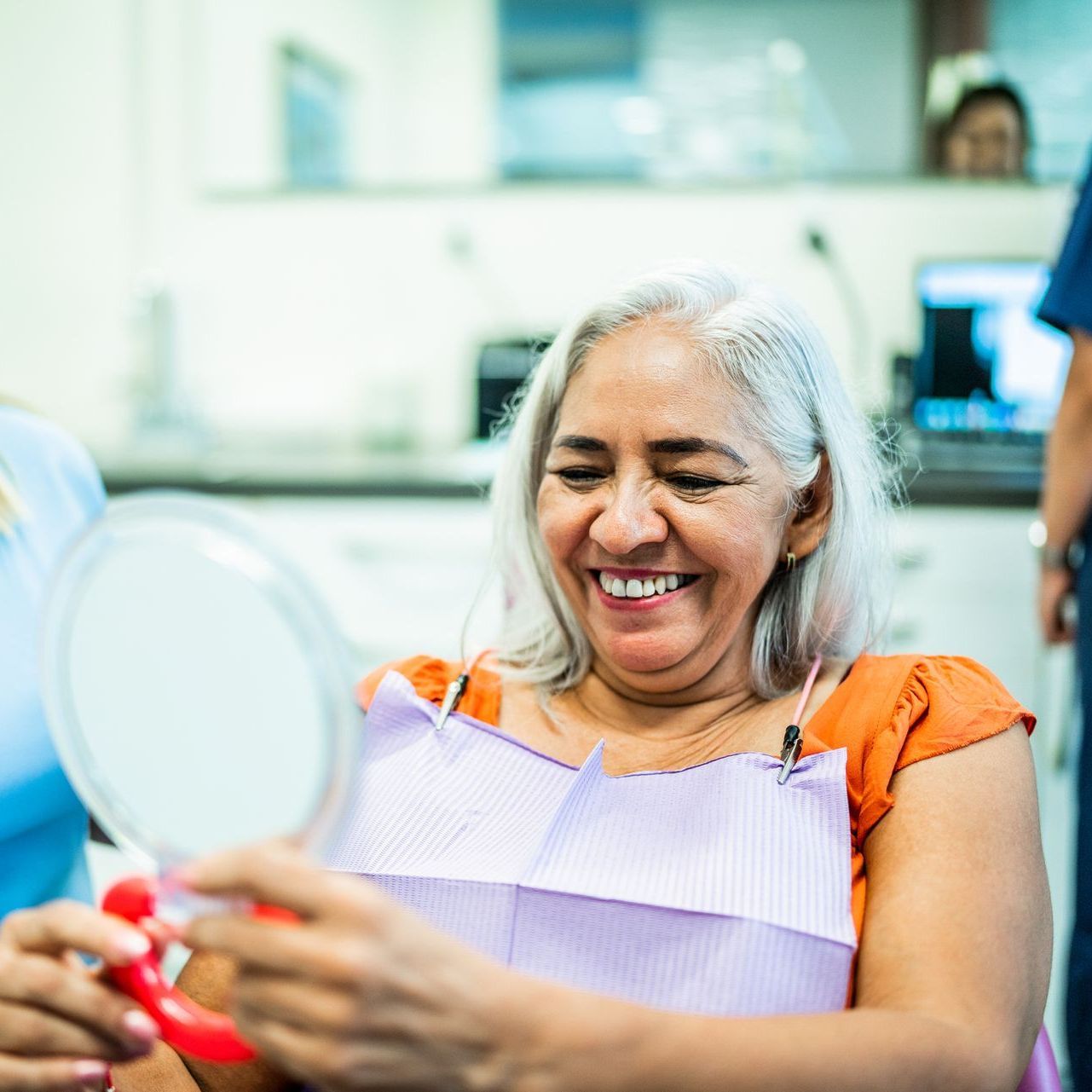 A woman is smiling while looking at her teeth in a mirror.