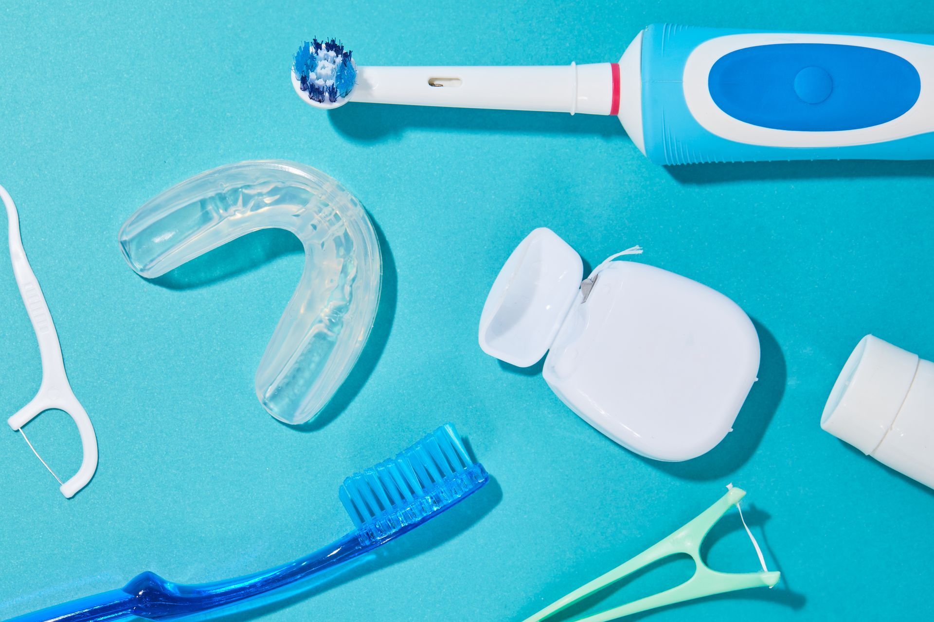 Dental hygiene tools, including toothbrush, floss, mouth guard, and whitening tube on a blue surface.