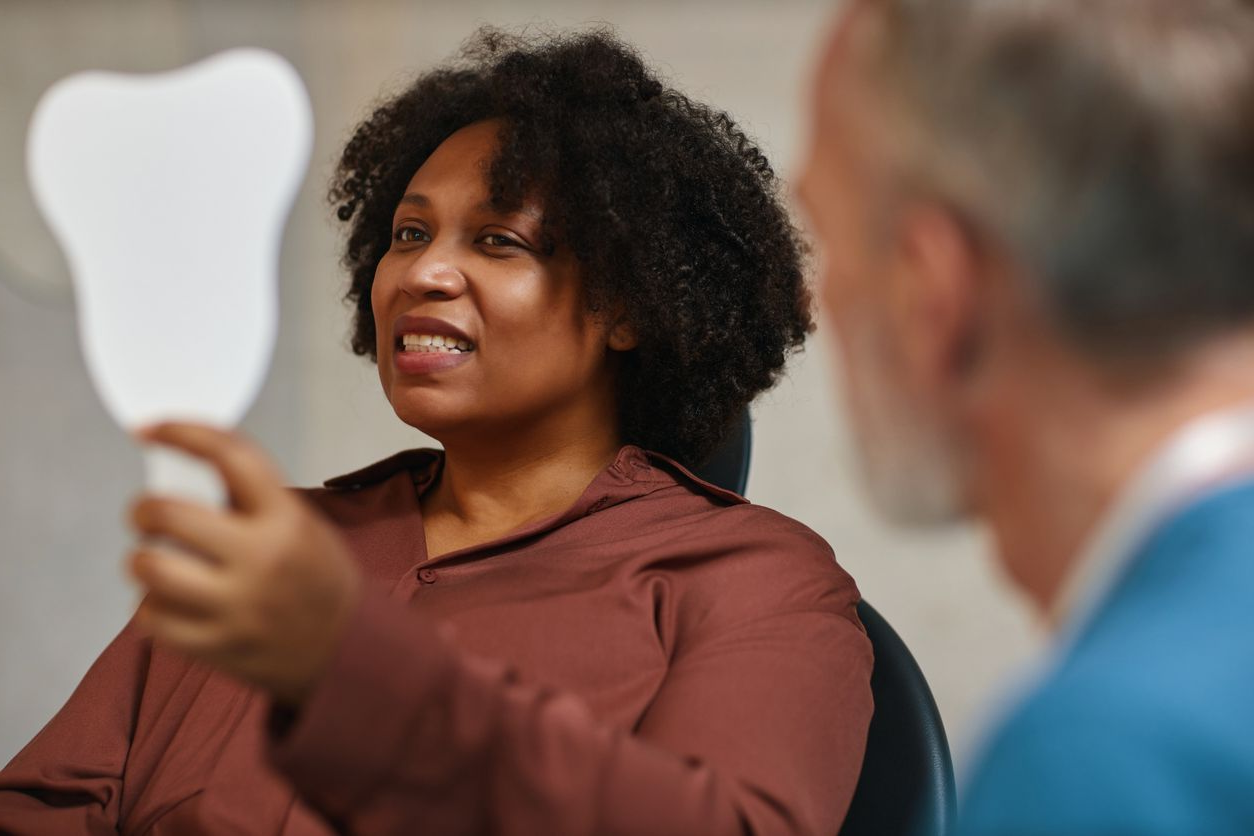 A woman is sitting in a dental chair looking at her teeth in a mirror.