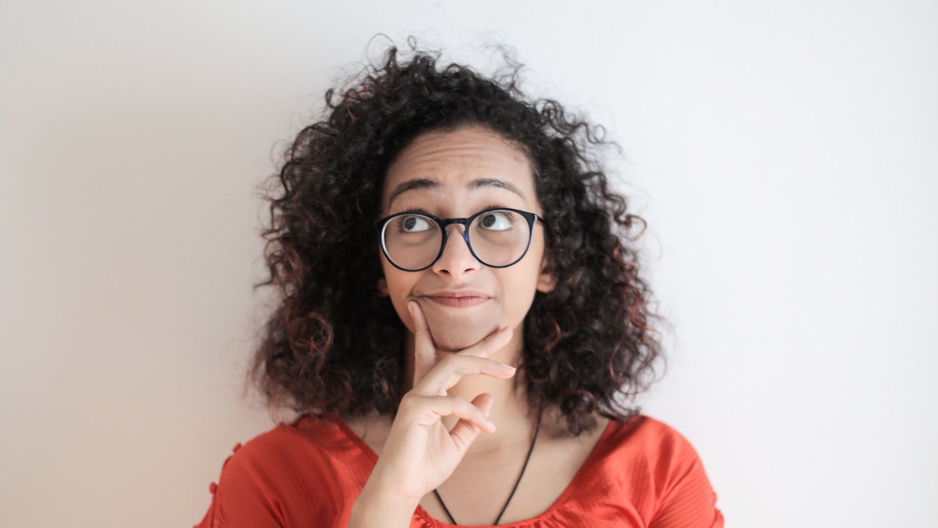 A woman with curly hair and glasses is thinking about something.