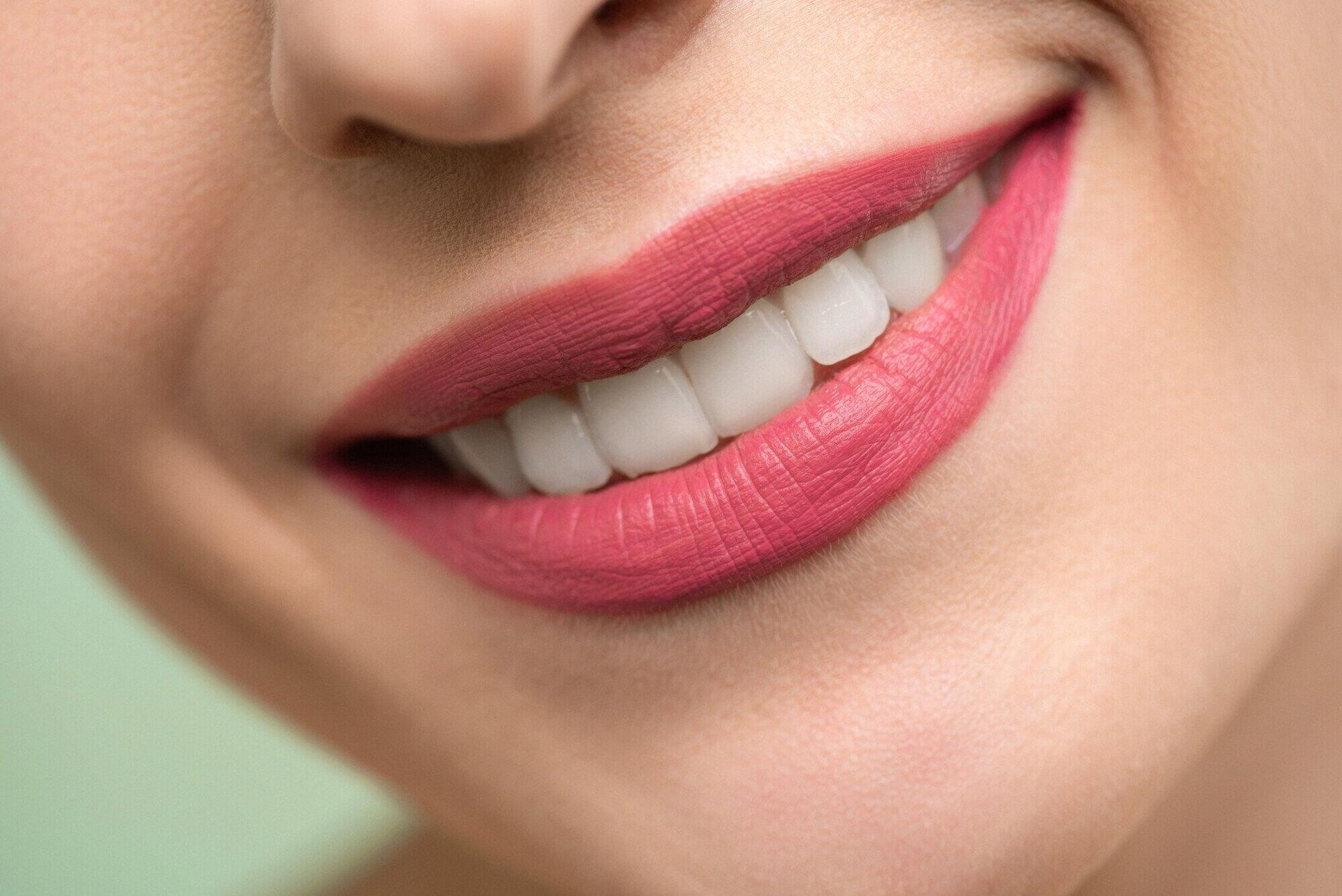 A close up of a woman 's smile with white teeth and red lipstick.