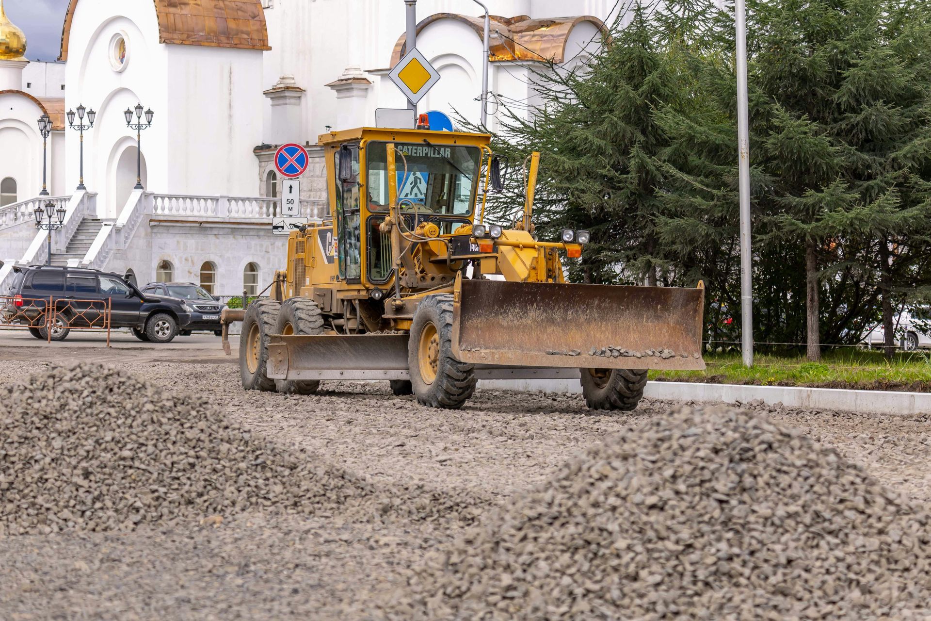 A yellow bulldozer is driving down a dirt road in front of a church.