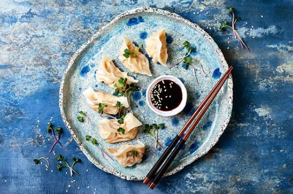 Ein Teller mit Teigtaschen mit Stäbchen und Dip-Sauce auf einem blauen Tisch.