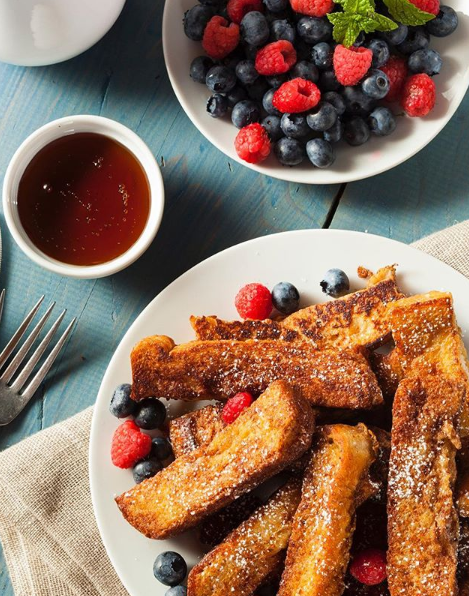 Zwei Teller French Toast mit Beeren und Sirup auf einem Tisch.