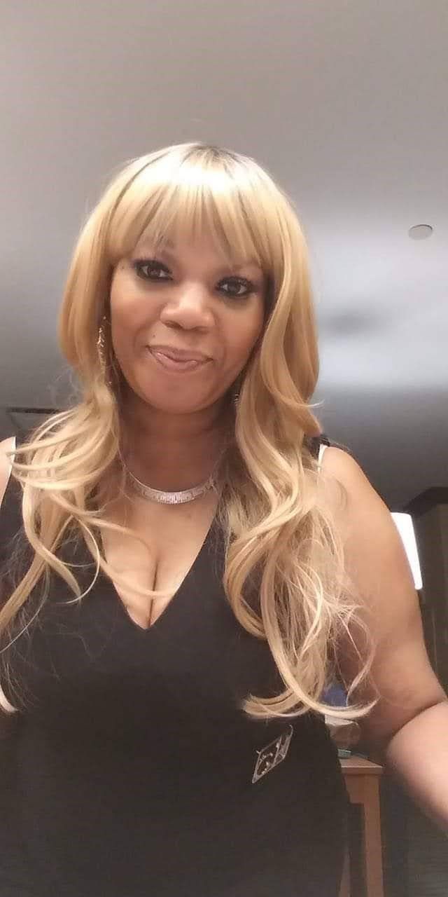 A woman with long blonde hair is wearing a black dress and a necklace.