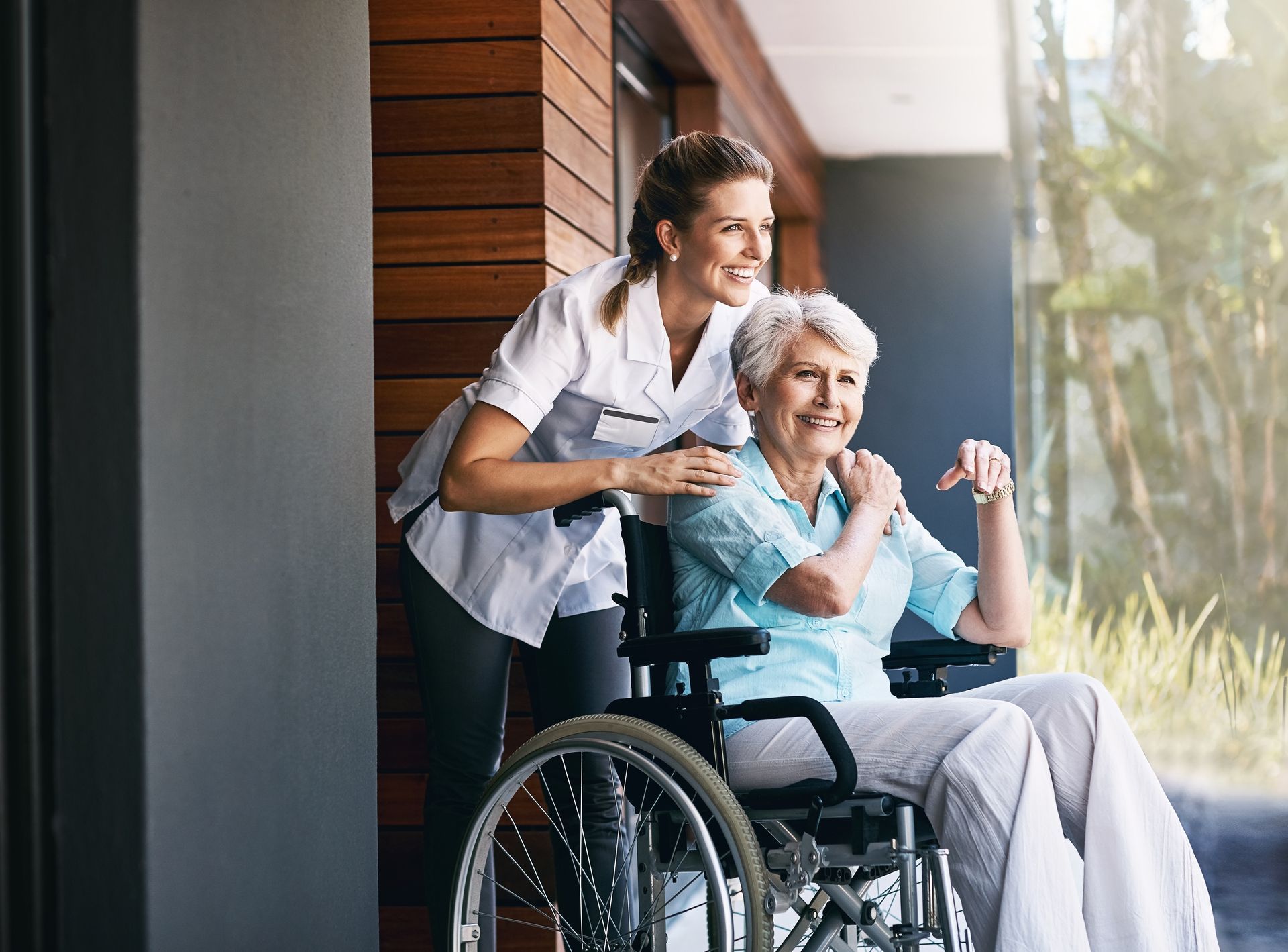 An elderly woman in a wheelchair is being helped by a nurse.