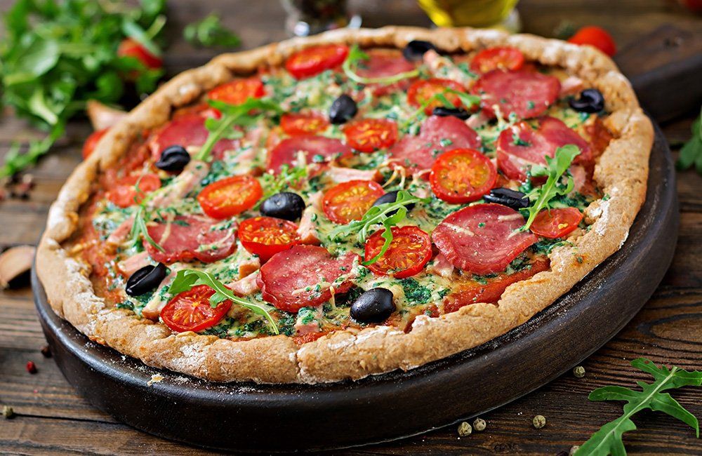 A pizza with tomatoes and olives on a wooden cutting board.