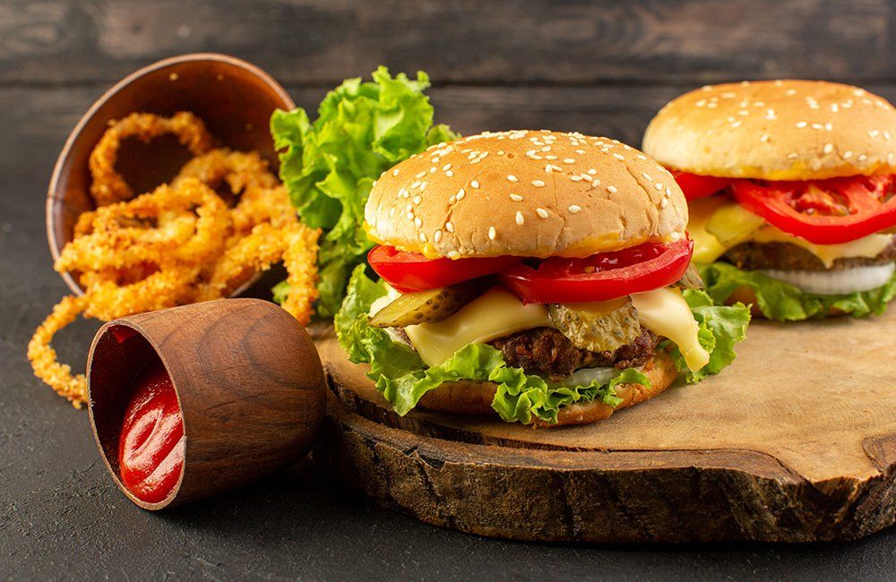 Two hamburgers and onion rings are on a wooden cutting board.