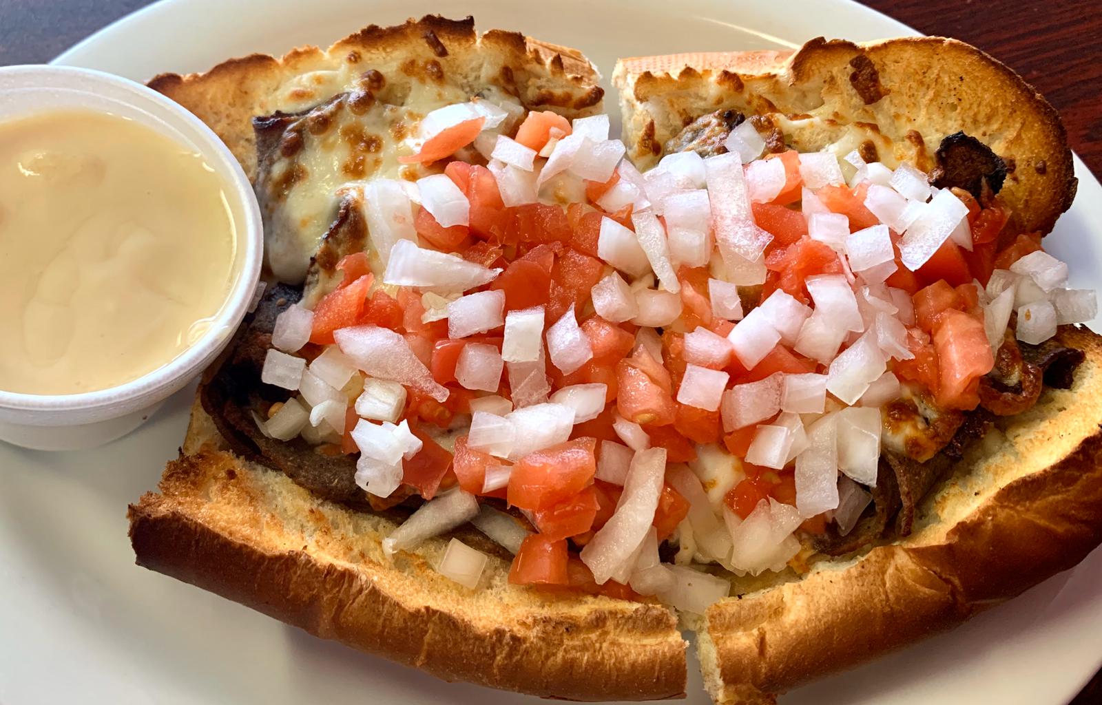 A sandwich with tomatoes and onions on it is on a plate with a dipping sauce.