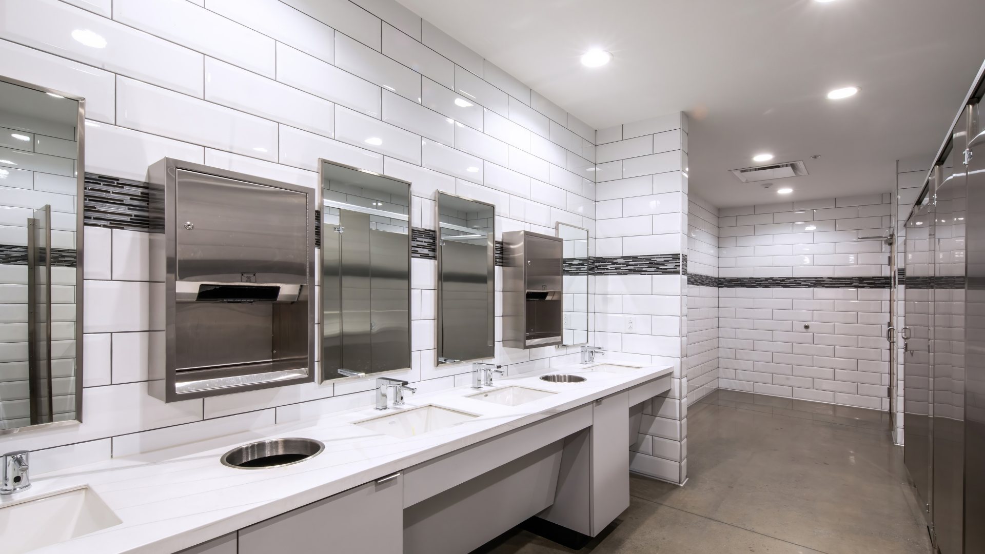Clean public restroom with white tiled walls, stainless steel fixtures, and sinks.