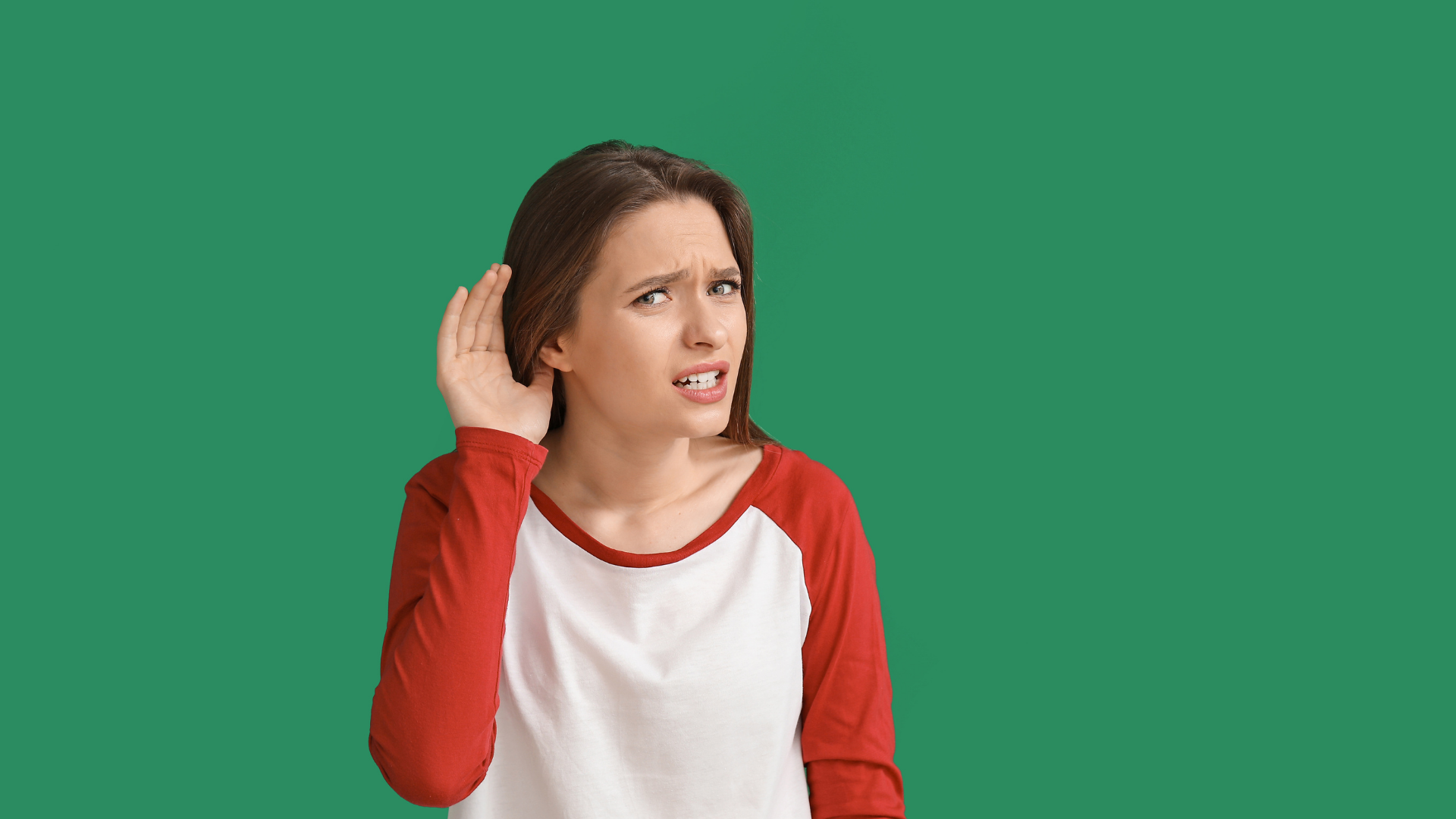 Woman with hand cupped to ear, listening intently with a puzzled expression against a green background.