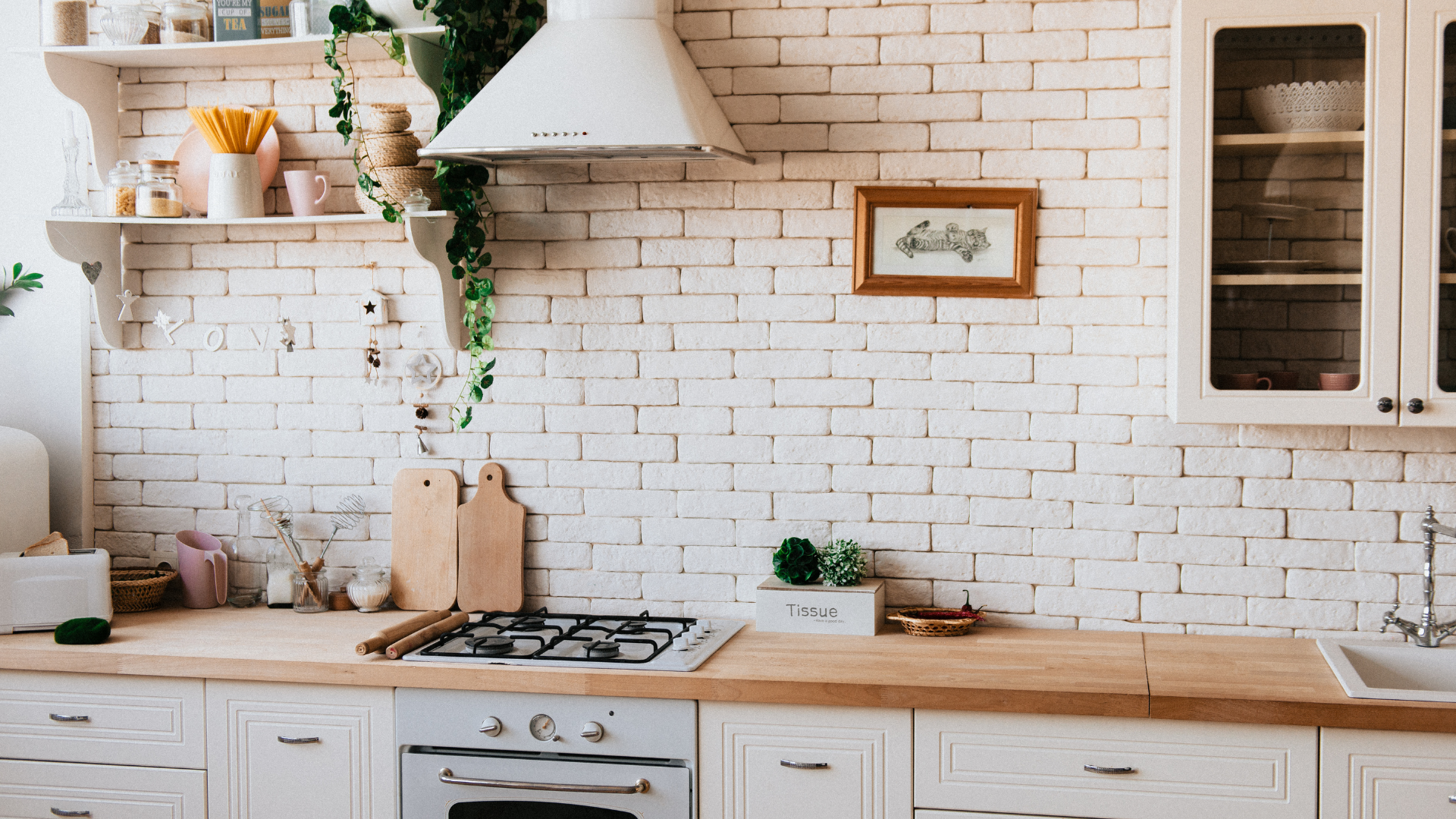 White brick kitchen with wooden countertops, gas stove, and hanging greenery.