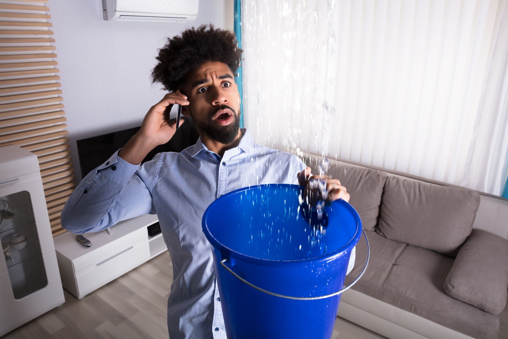 A man holding a bucket catching leaks from the ceiling