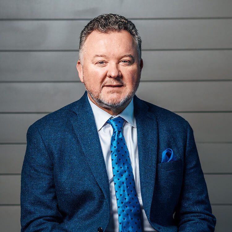 A man in a suit and tie is sitting in front of a wall.