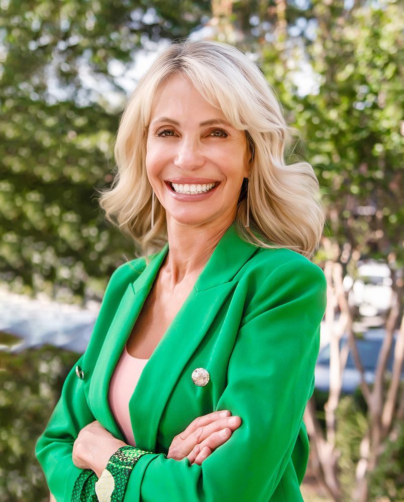 A woman in a green jacket is smiling with her arms crossed.