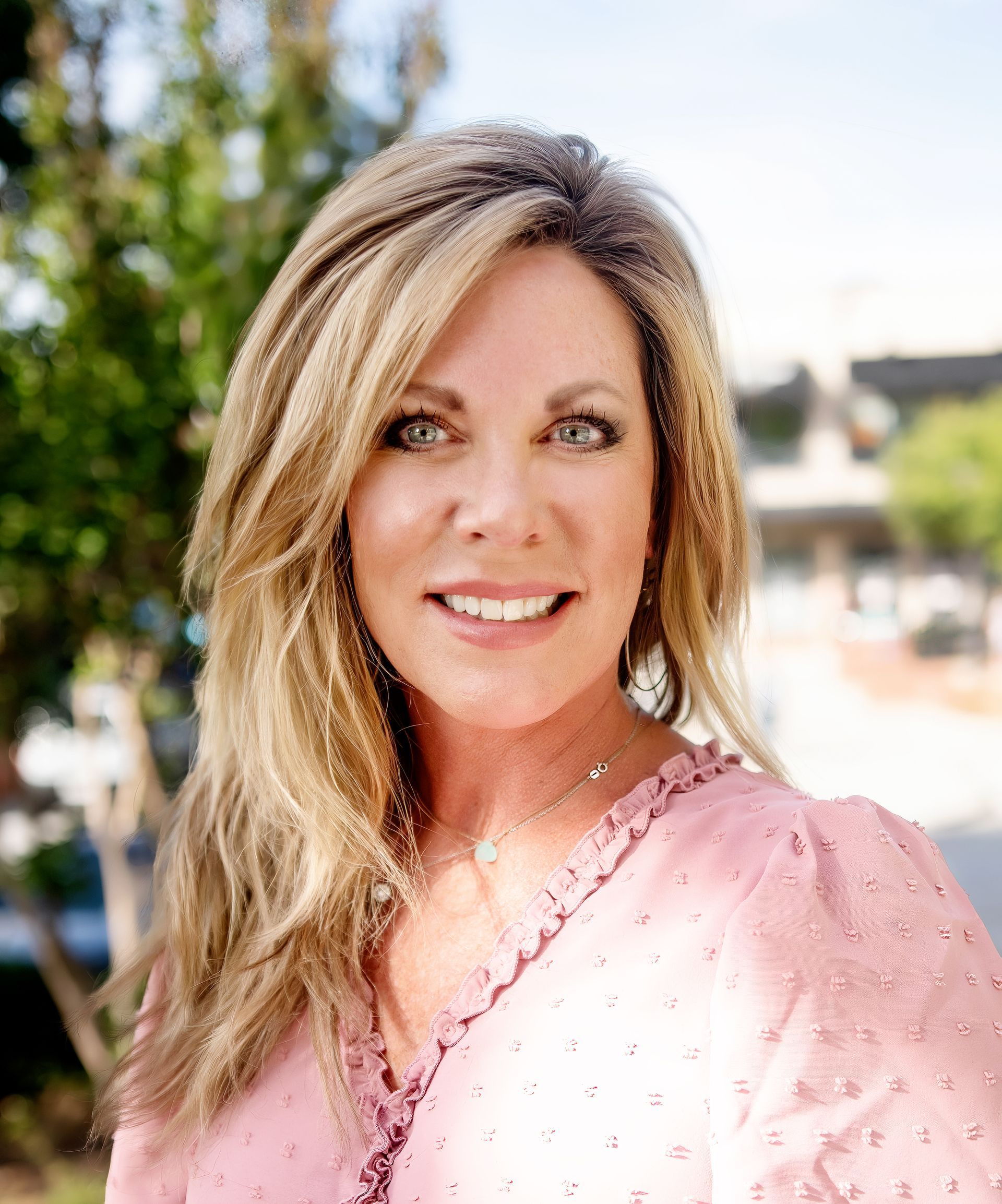A woman in a pink shirt is smiling for the camera.