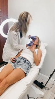 A woman is laying on a bed getting a facial treatment from a doctor.