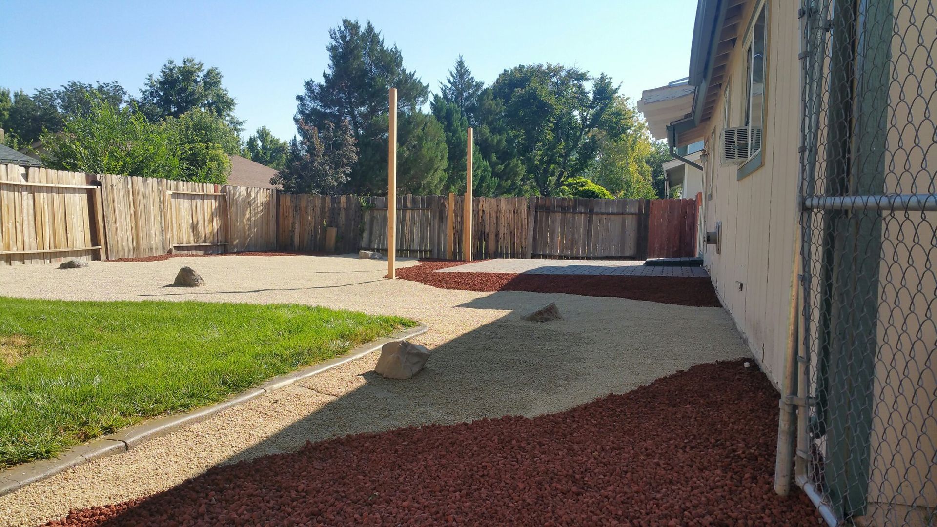 A backyard with a fence and gravel and a house in the background