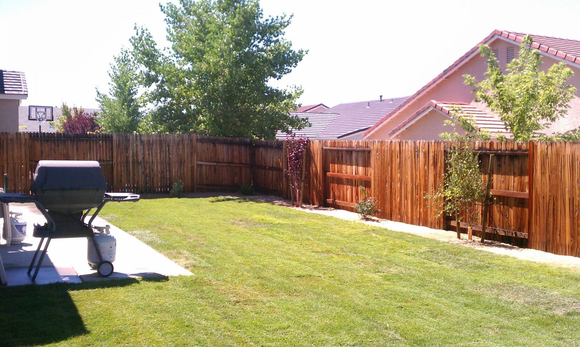 A backyard with a wooden fence and a grill