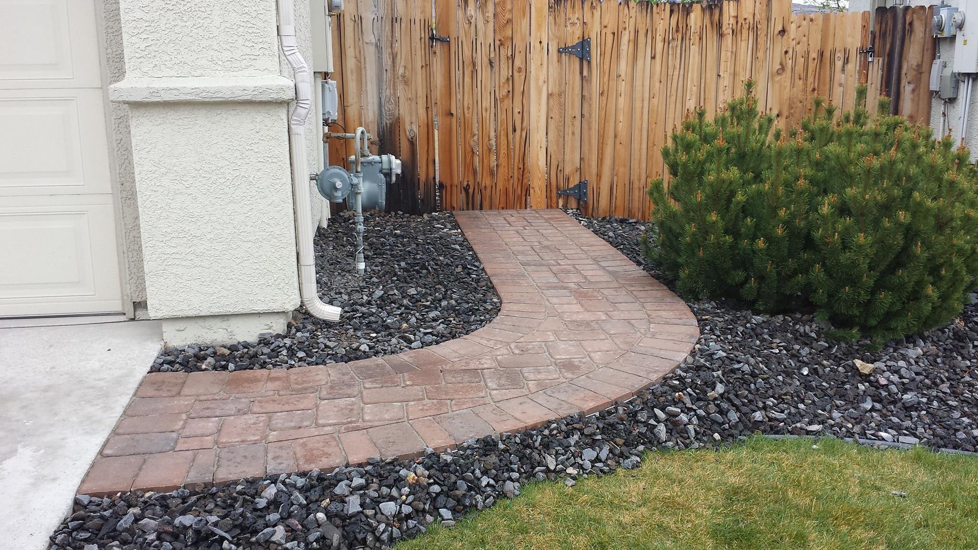 A brick walkway leading to a wooden fence in a yard.