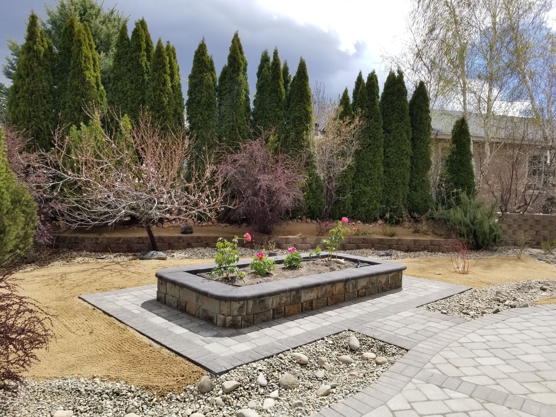 A garden with a stone planter filled with flowers and trees in the background.