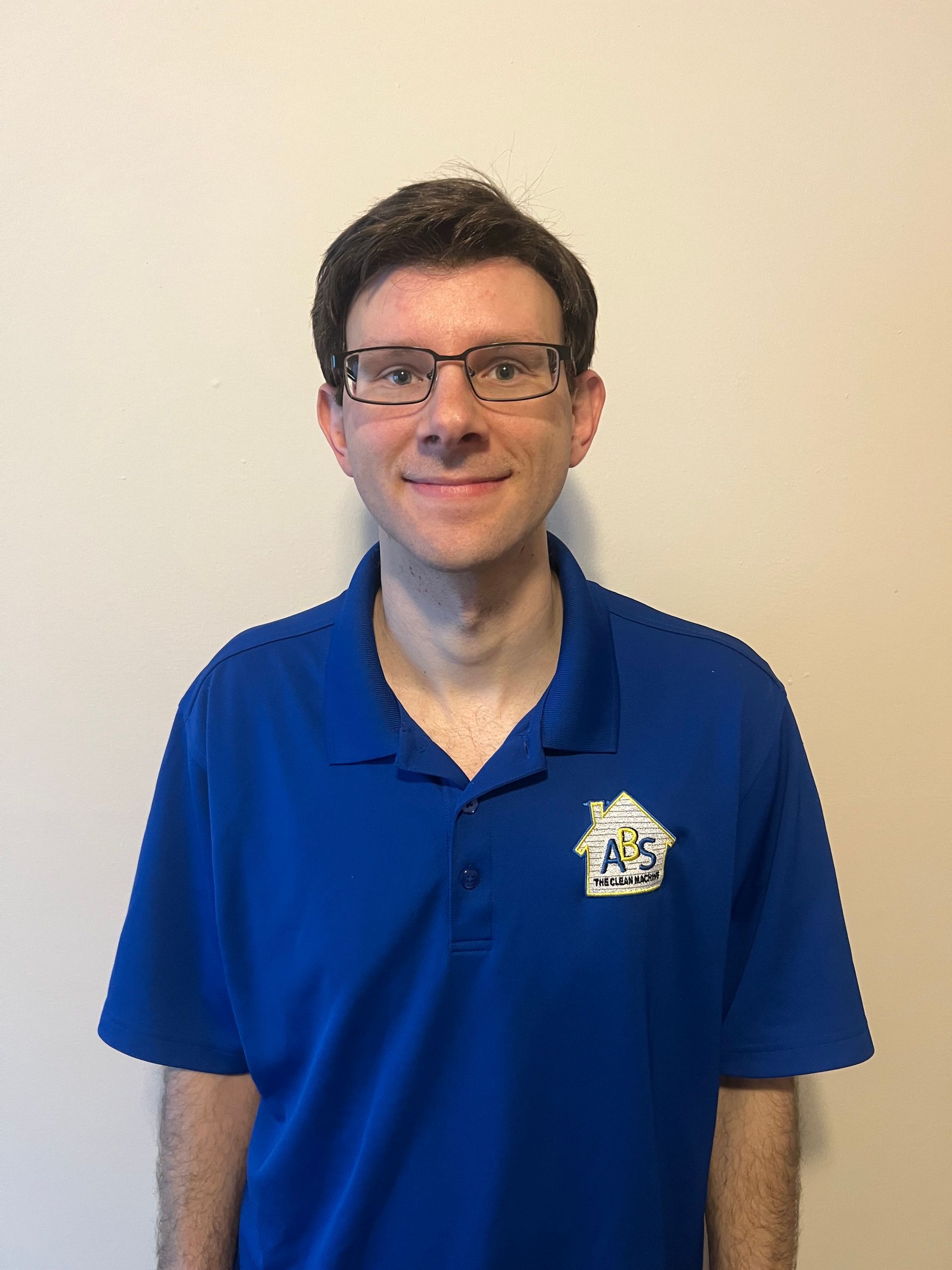 Man with glasses wearing a blue polo shirt smiles, stands against beige siding. Man with glasses wearing a blue polo shirt smiles, stands against beige siding.