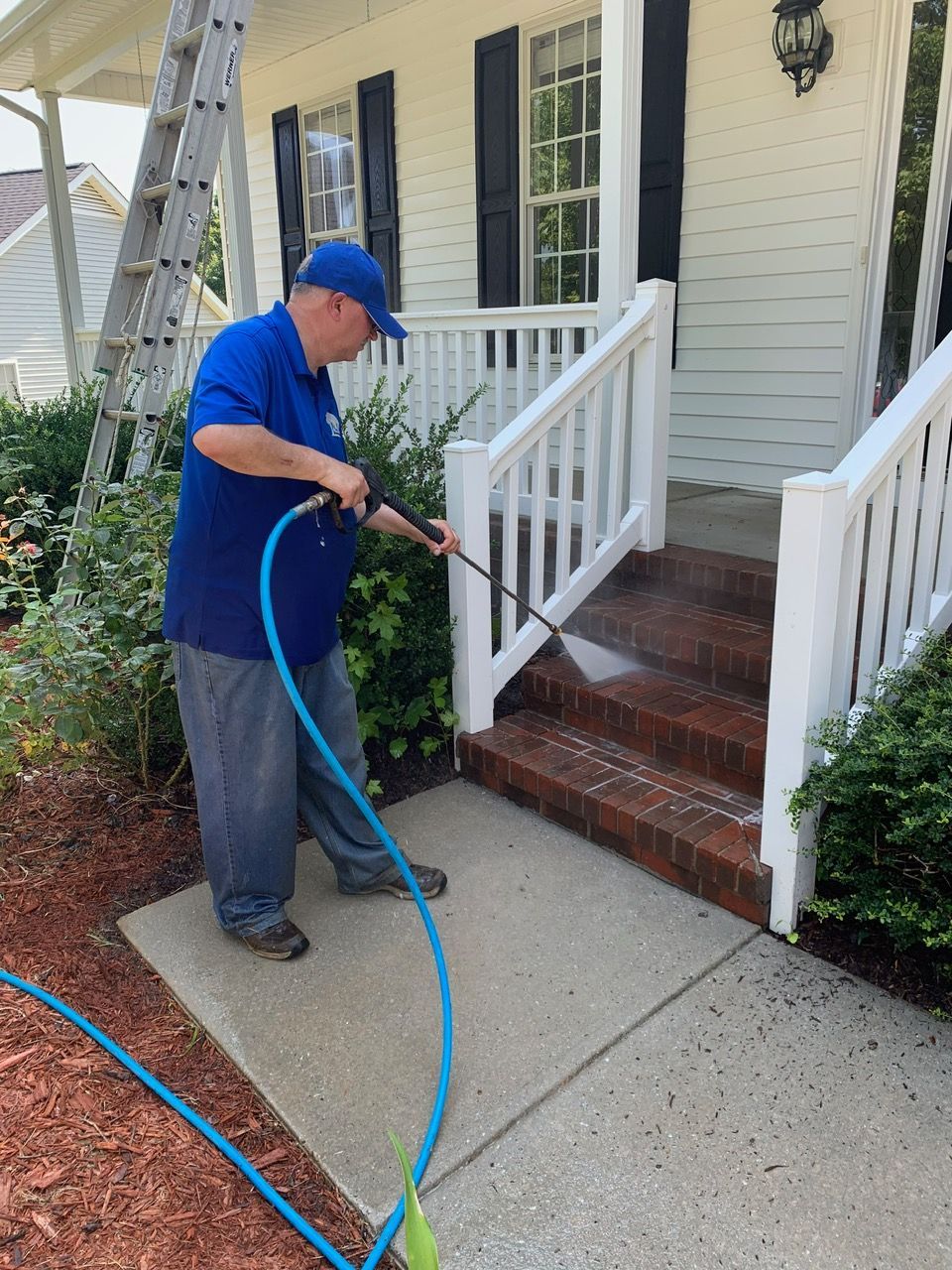 Person in blue coveralls pressure washing a concrete surface, water spraying.