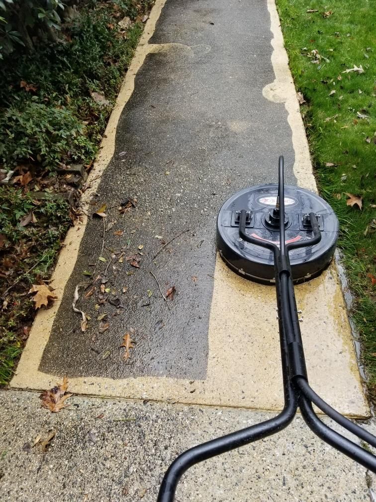 A power washer cleaning a concrete sidewalk. Half is clean, half is dirty.