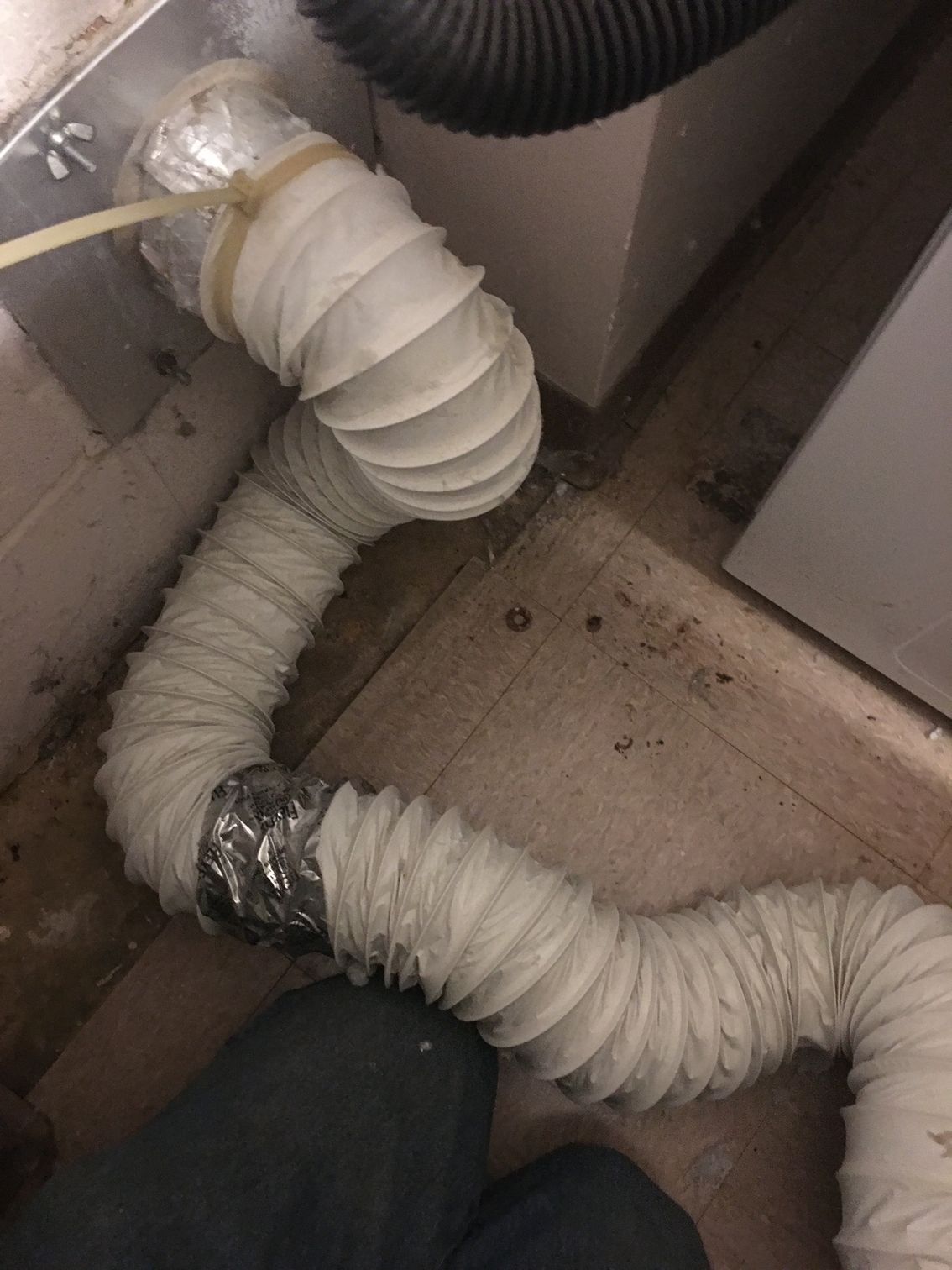 White dryer vent hose, connected to an appliance, snaking across a dirty floor.