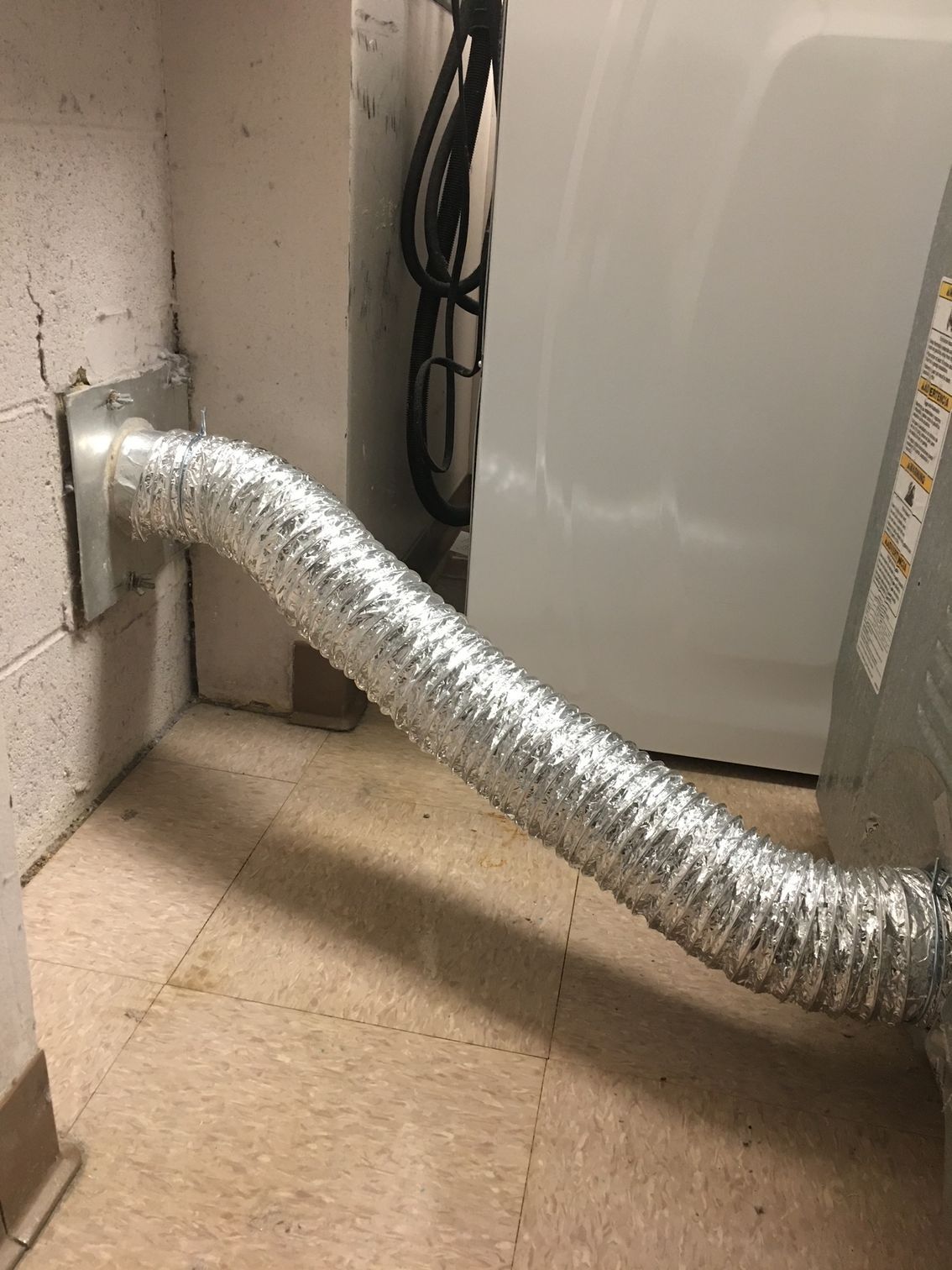 Person vacuuming a white wall vent with a black hose.