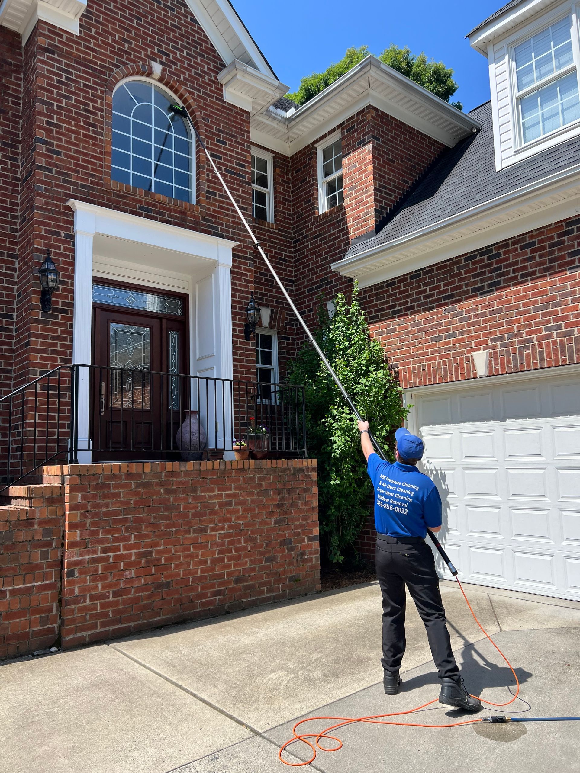 Person wearing gloves cleans a brown table with a blue cloth and spray bottle, near a sofa.