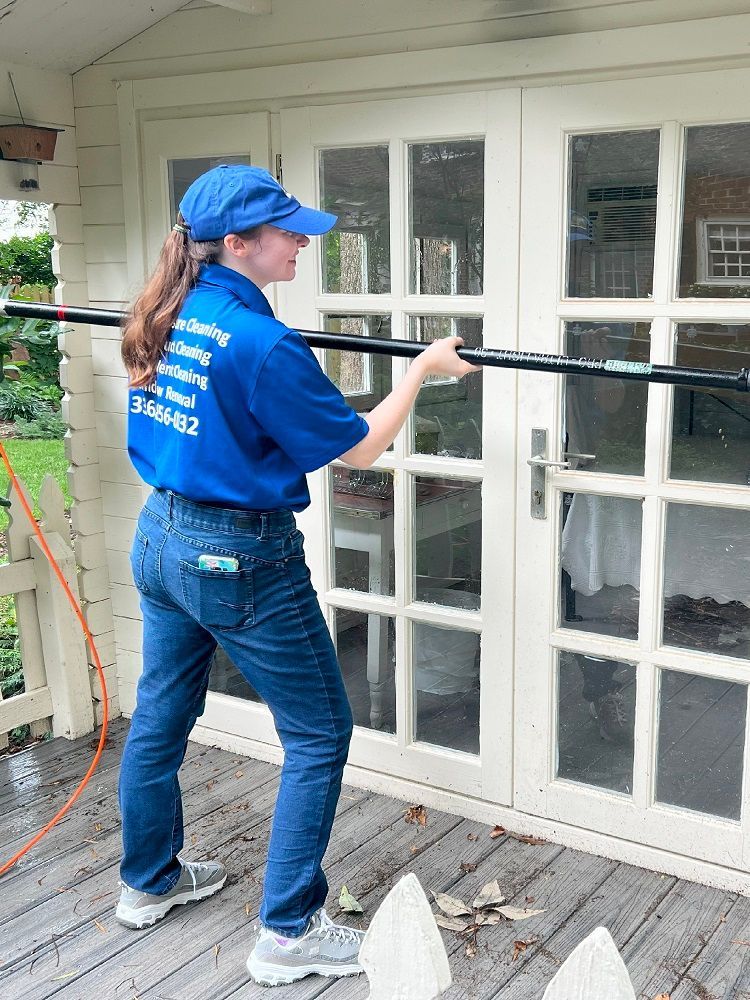 Woman cleaning French doors with a long-handled tool; blue shirt, jeans, and cap. Woman cleaning French doors with a long-handled tool; blue shirt, jeans, and cap.