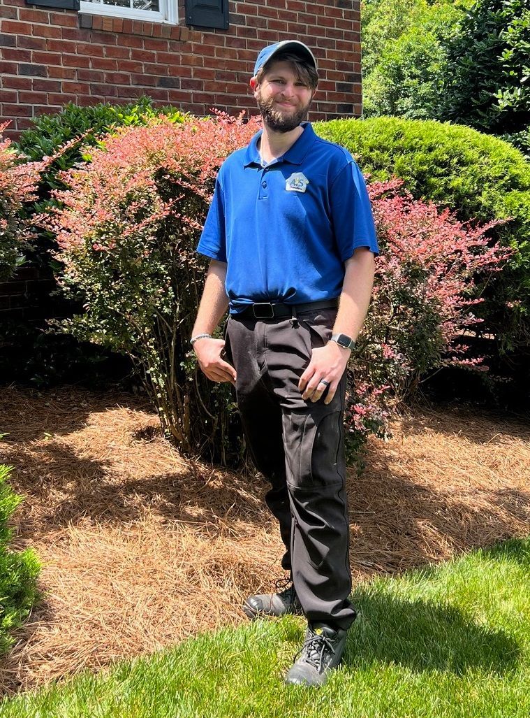 Man in blue shirt and black pants standing outside in front of shrubs. Man in blue shirt and black pants standing outside in front of shrubs.