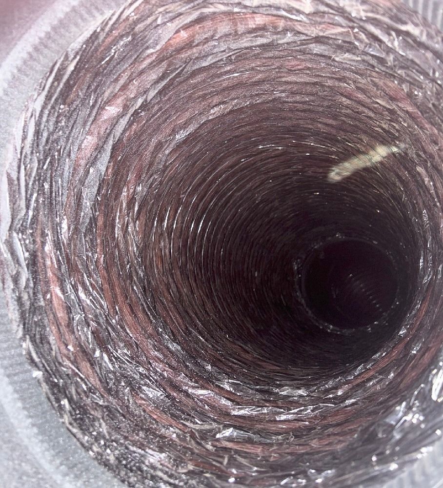 Inside view of a flexible metallic duct, showing ridges and some debris.
