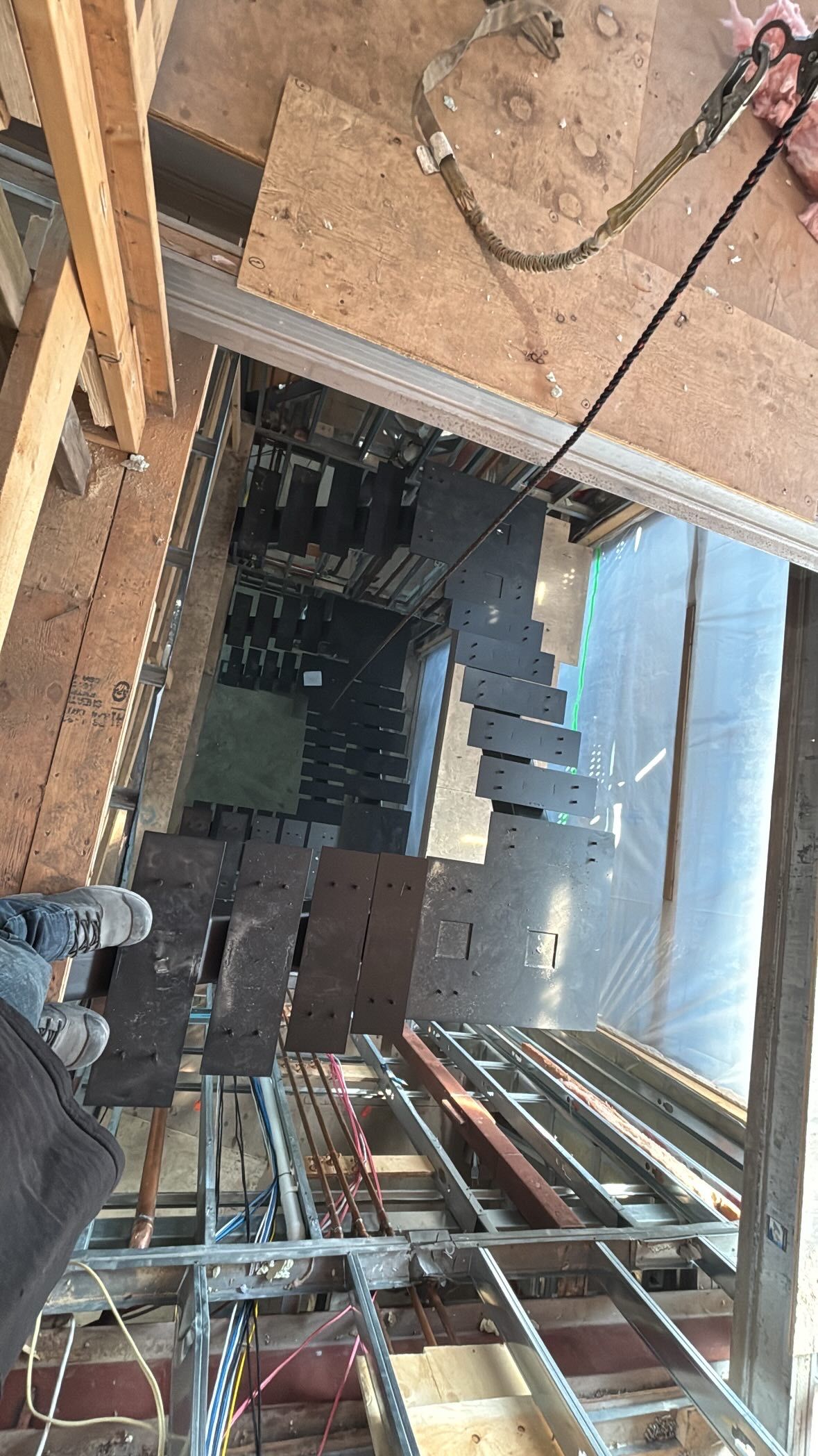 Vue plongeante depuis un toit, montrant des tuiles partiellement posées, des poutres de soutien et des équipements de sécurité.