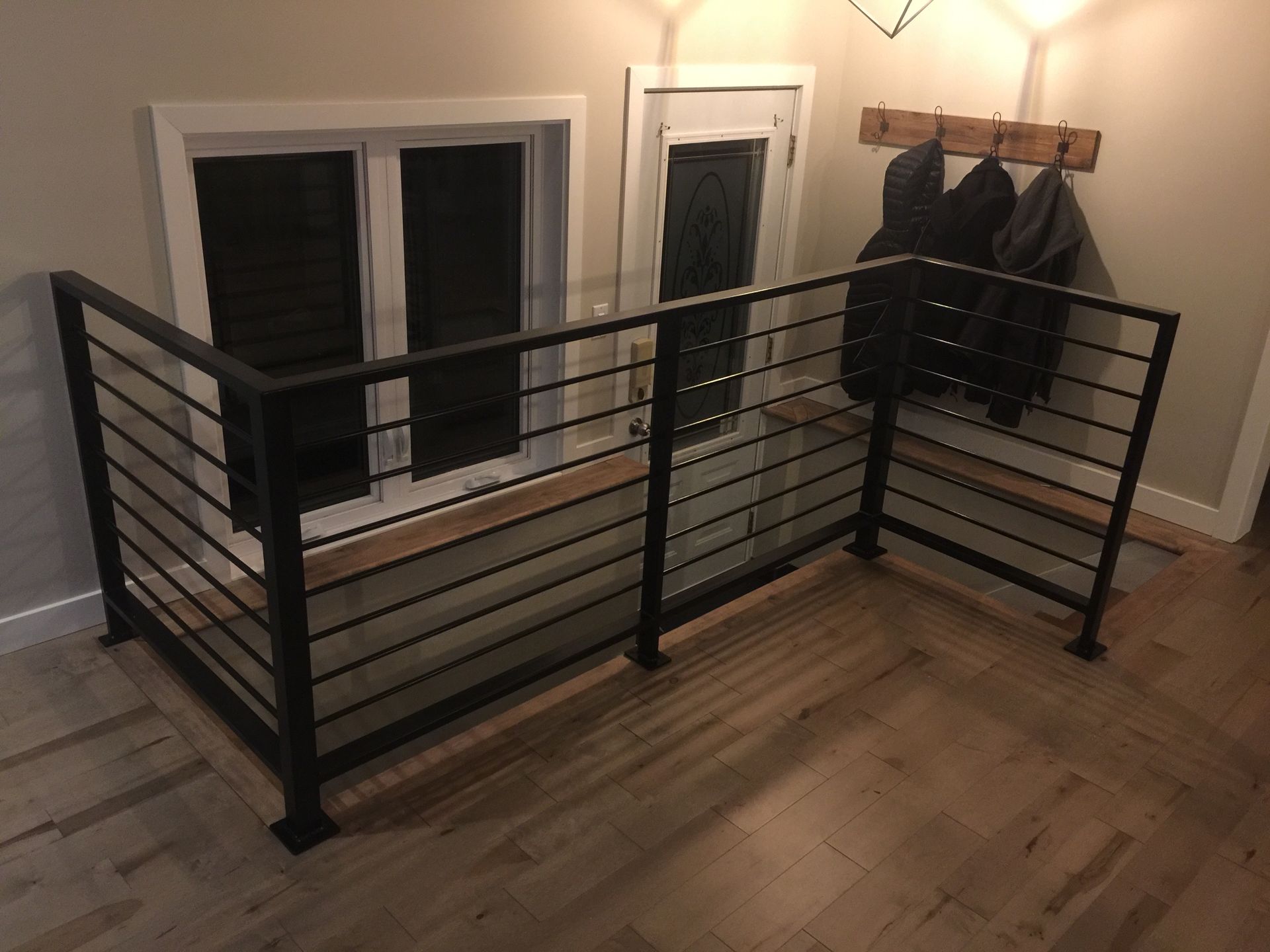Rambarde en métal noir sur un plancher en bois, près d'une fenêtre et d'un porte-manteau.