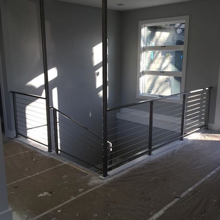 Vue intérieure d'un escalier avec des murs gris, une rampe en câbles d'acier inoxydable et une fenêtre.