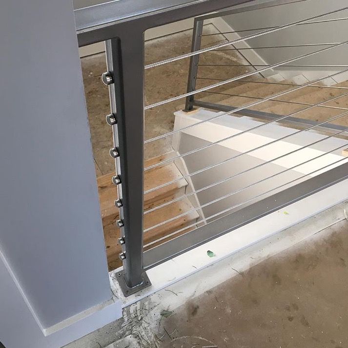 Rambarde métallique à câbles d'acier horizontaux sur un escalier. Intérieur gris et blanc, style moderne.