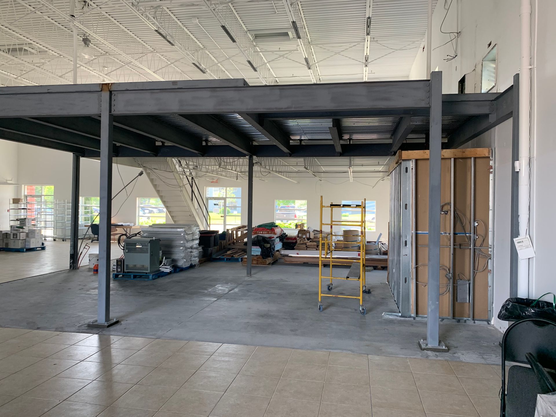Vue intérieure d'un bâtiment en construction, montrant une mezzanine métallique, un escalier et divers matériaux de construction.