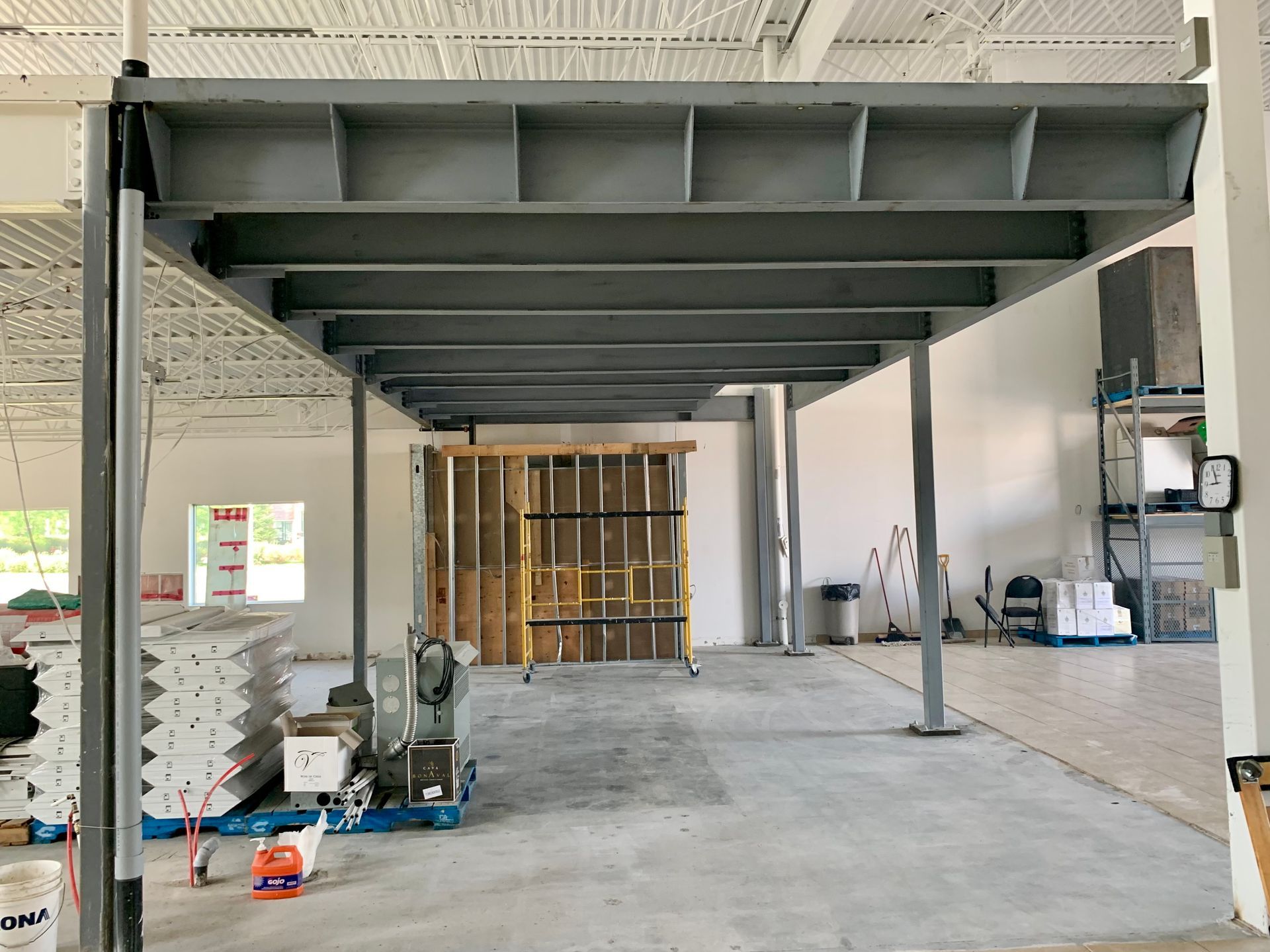 Intérieur d'un bâtiment en construction, montrant une structure de mezzanine métallique soutenue par des colonnes.