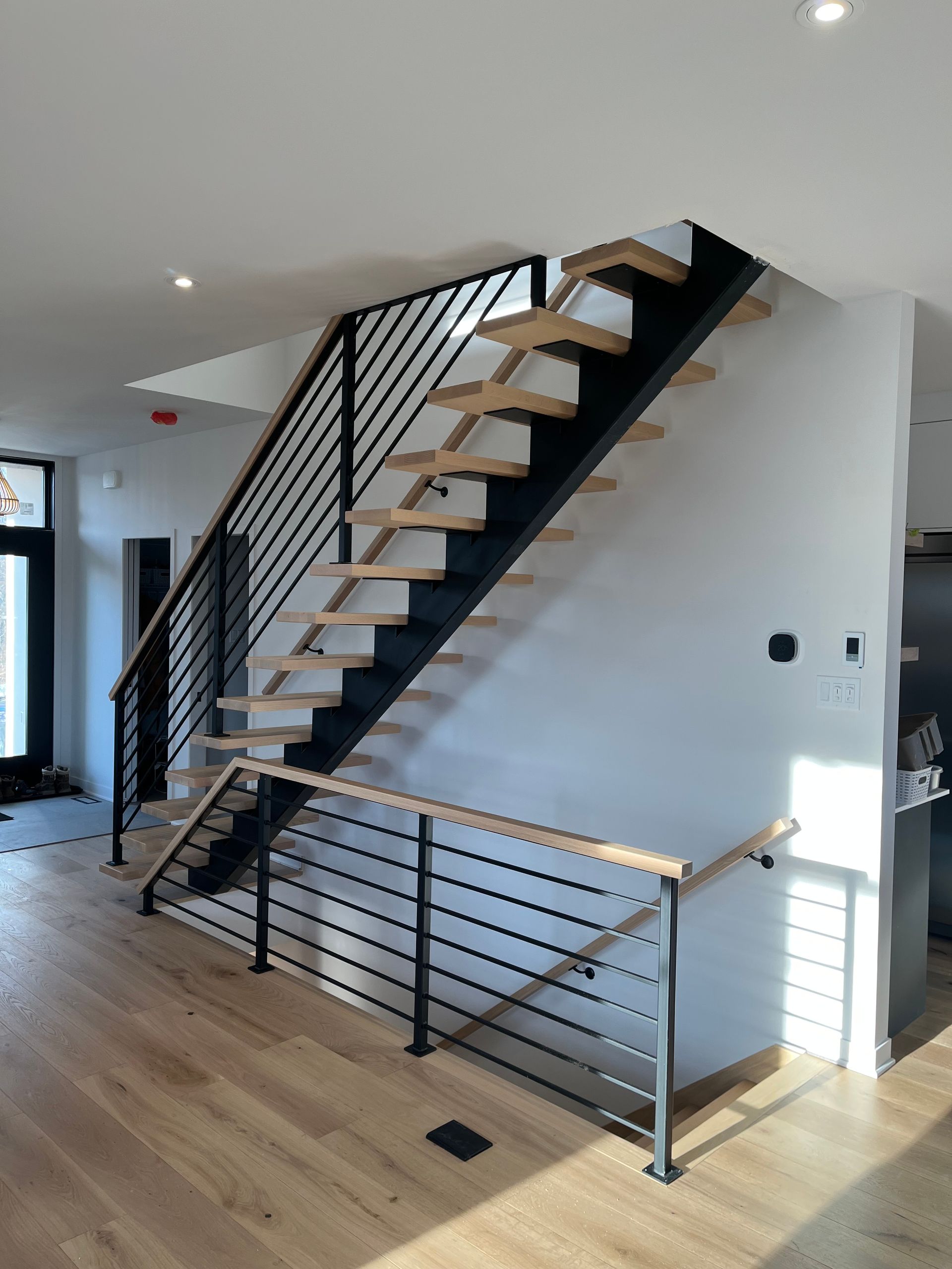 Escalier moderne avec rampes en métal noir, marches en bois clair et main courante en bois.