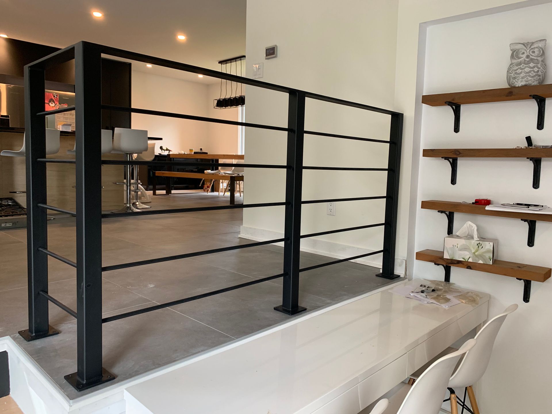 Rambarde en métal noir sur une plateforme surélevée, avec étagères et chaises blanches visibles.