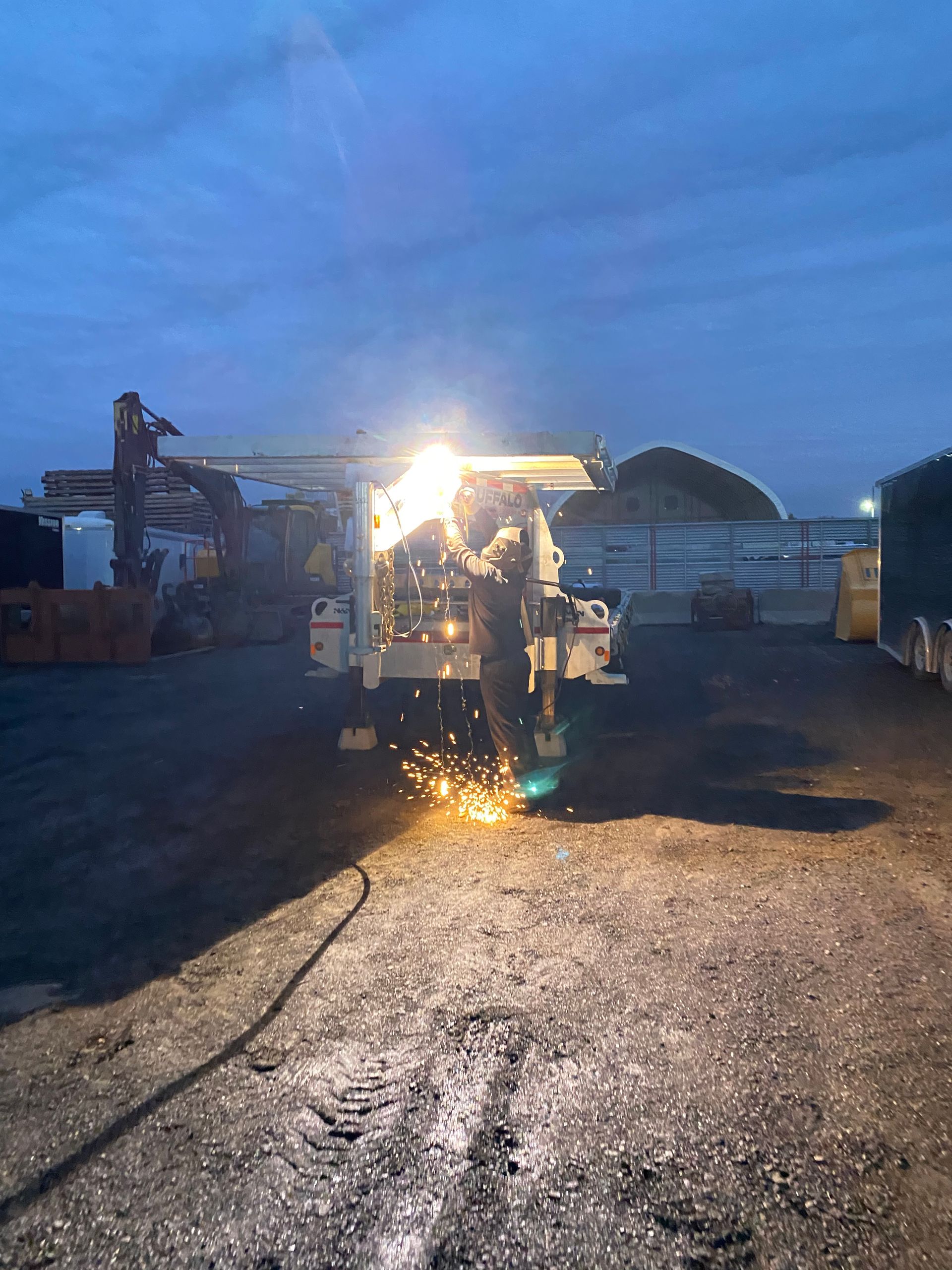 Un homme soude sur une machine à l'extérieur au crépuscule, des étincelles volent.
