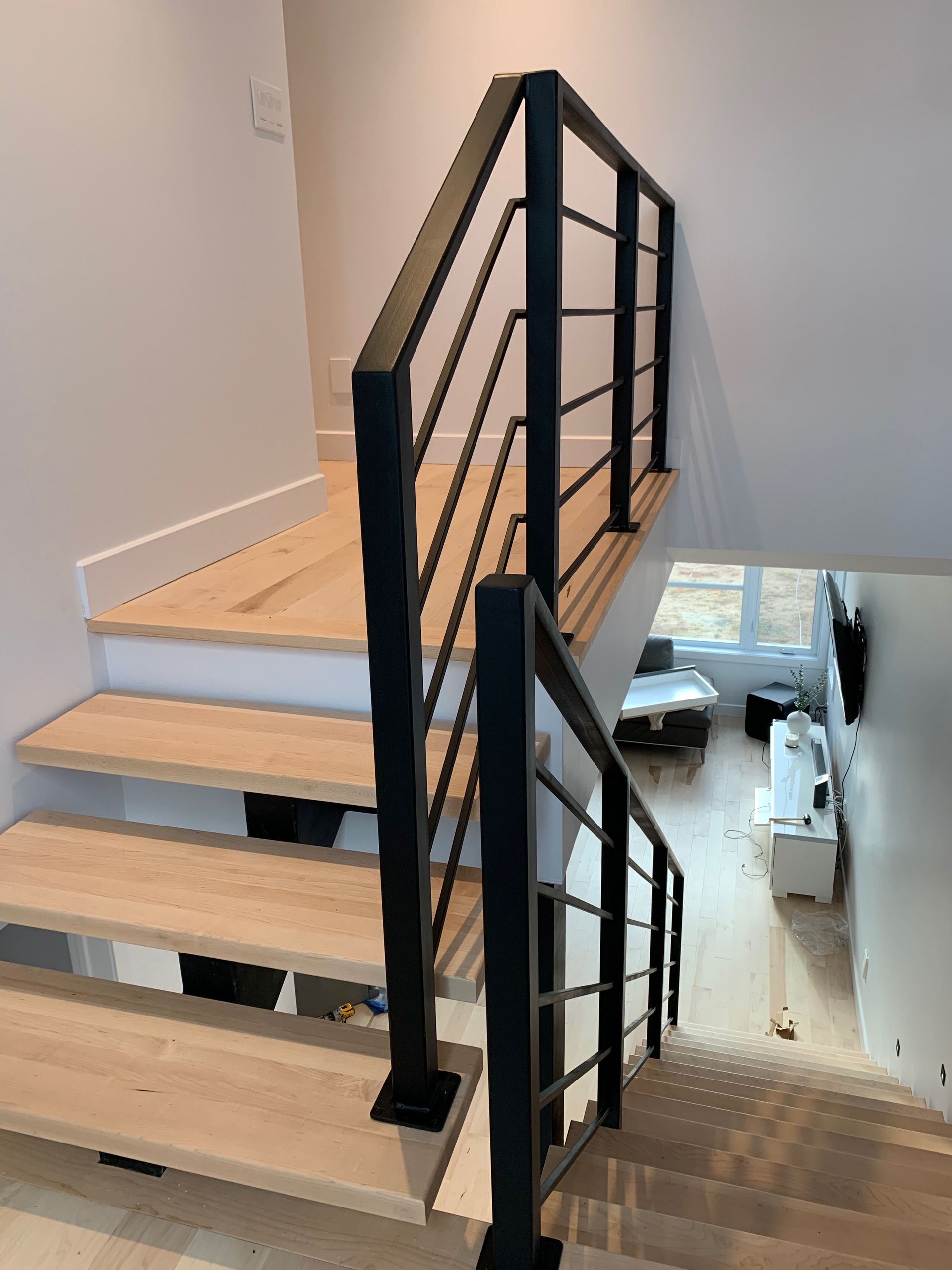 Escalier avec marches en bois et rampe en métal noir dans une maison moderne.