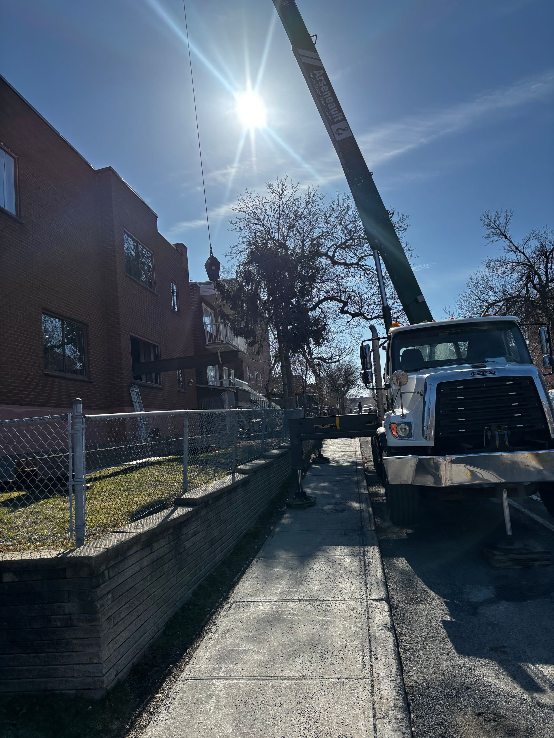 Un camion-grue élague un arbre près d'un bâtiment en briques par une journée ensoleillée.