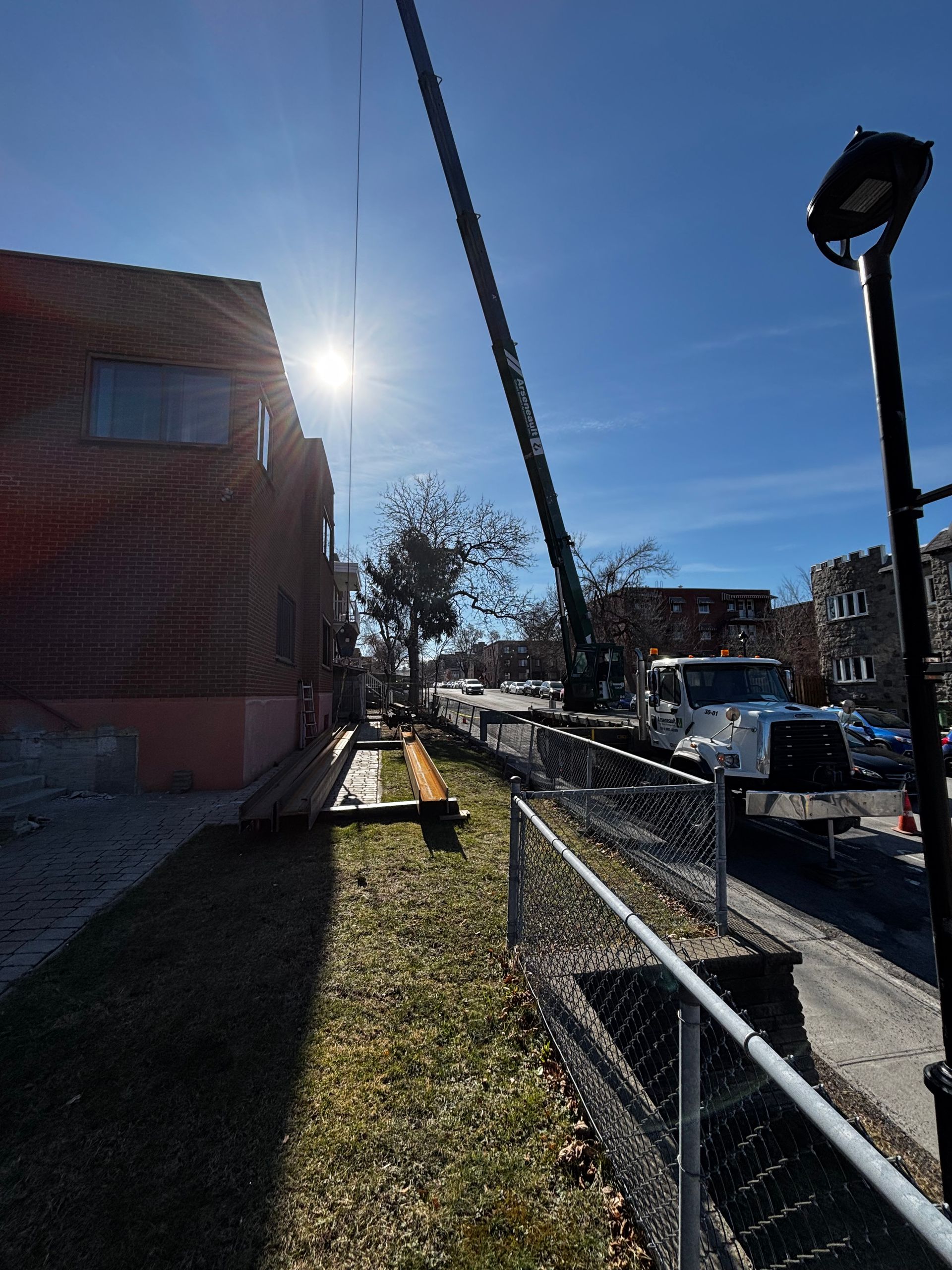 Grue au-dessus d'un bâtiment, ciel dégagé. Matériaux de construction au sol, journée ensoleillée.