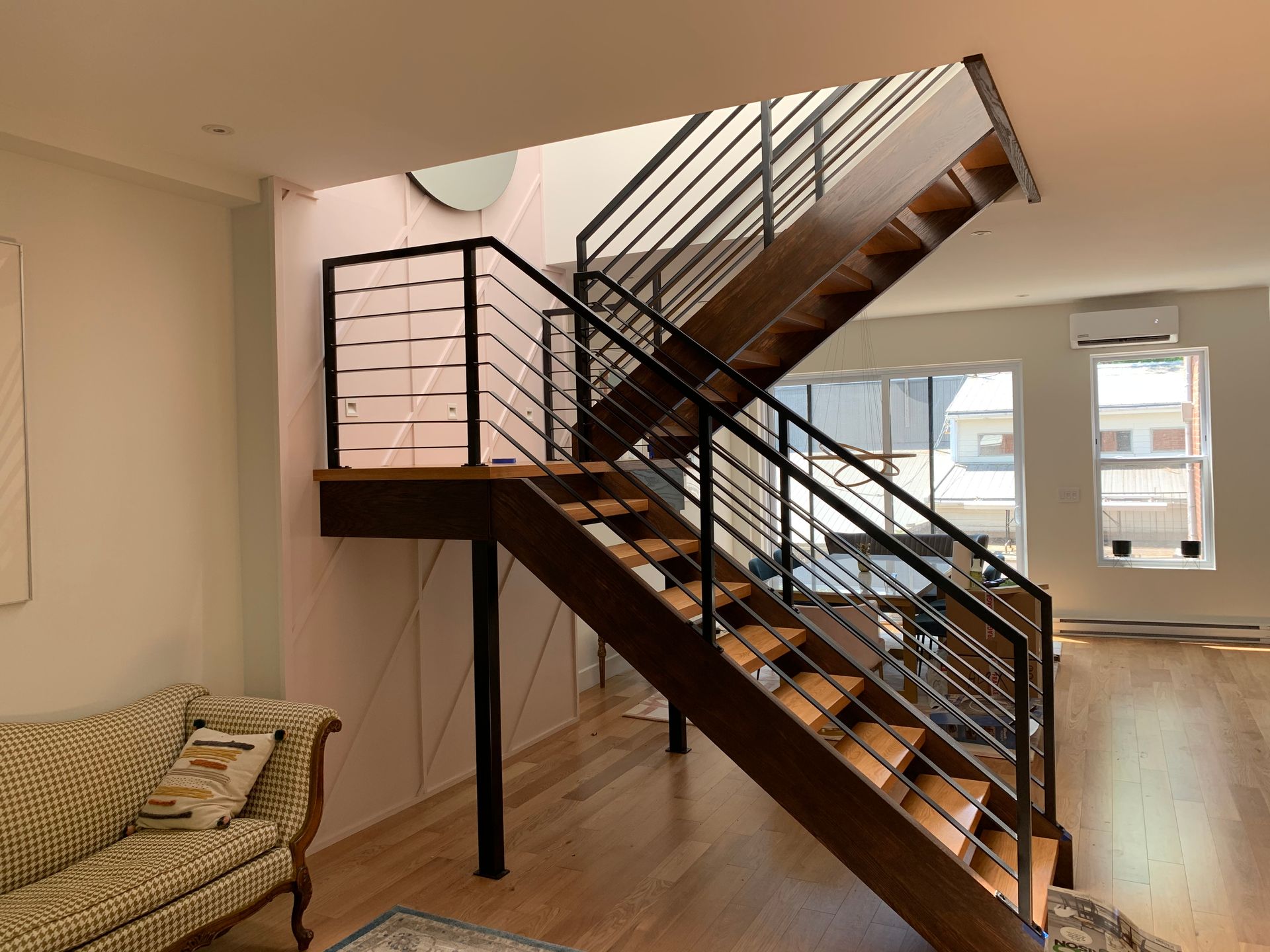 Escalier en bois avec rampes en métal noir dans une maison moderne et bien éclairée.